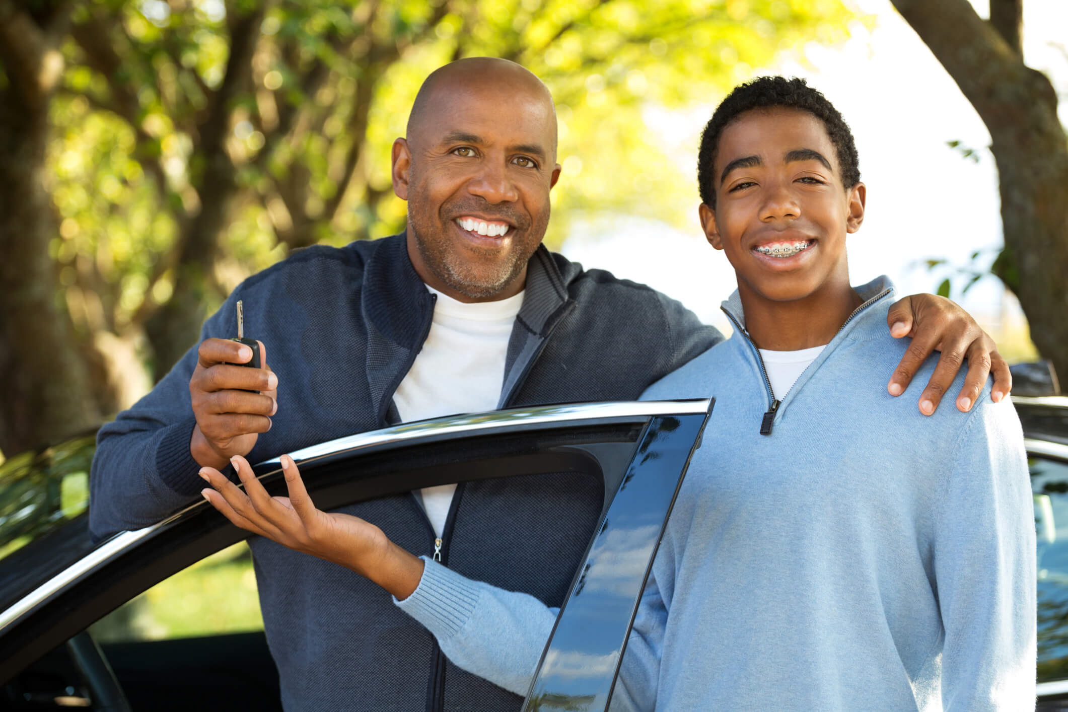a father and son pose as the father gives his son the keys to his car